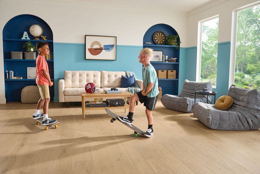 Two young boys riding skateboards in a living room area to show the resilience of engineered hardwood
