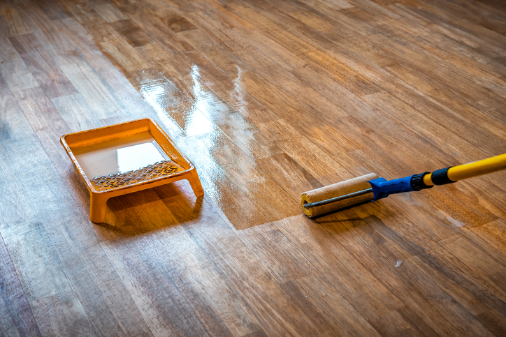Closeup of a wood floor with a brush and tray for refinishing the floor