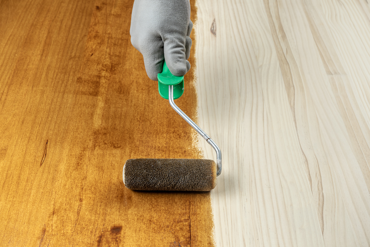 Closeup of a person using a roller to add stain to an unfinished wood floor