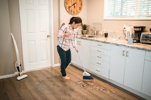 Woman sweeping wood flooring in a kitchen as one step in caring for wood floors